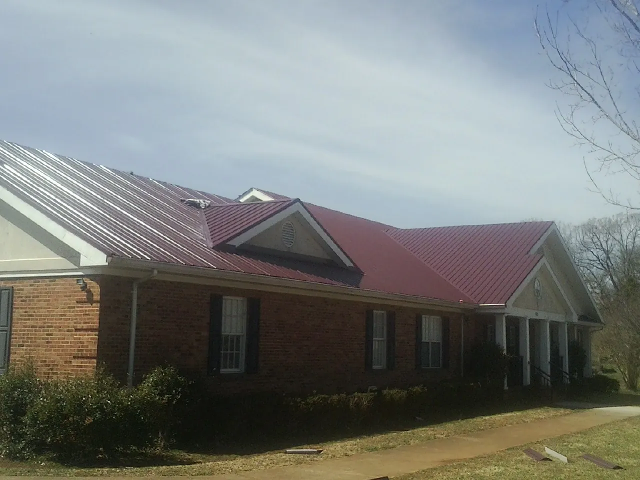 Red metal roof with gabled entries on a long brick building, from a Hail Damage Roof Repair job in Covington