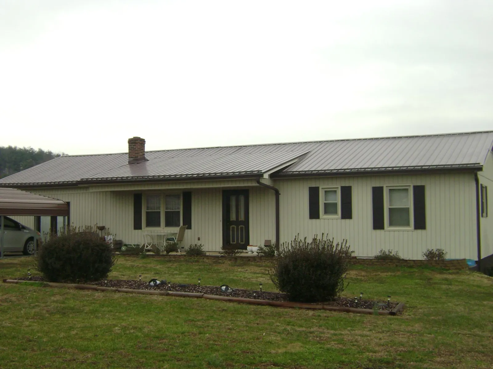 Brown metal roof on a cream sided ranch home with a brick chimney in Covington